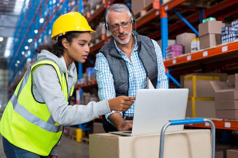 Warehouse manager and female worker using laptop in warehouse